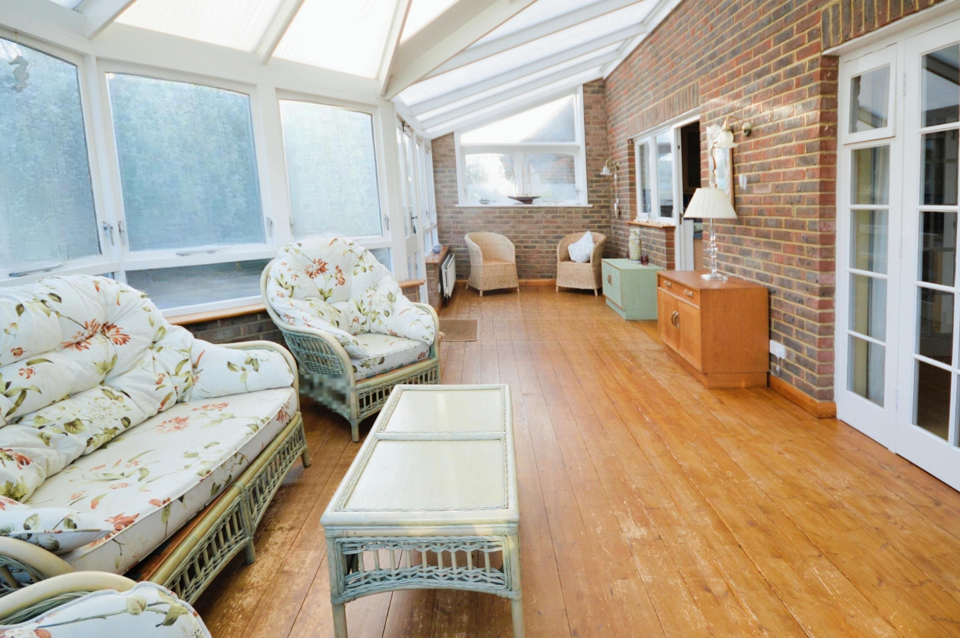 A sunroom with wicker furniture, a wooden table, and a brick wall.