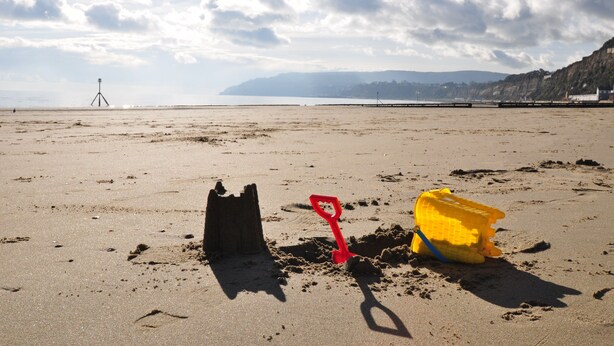 Una playa arenosa con una pala roja y un cubo amarillo.