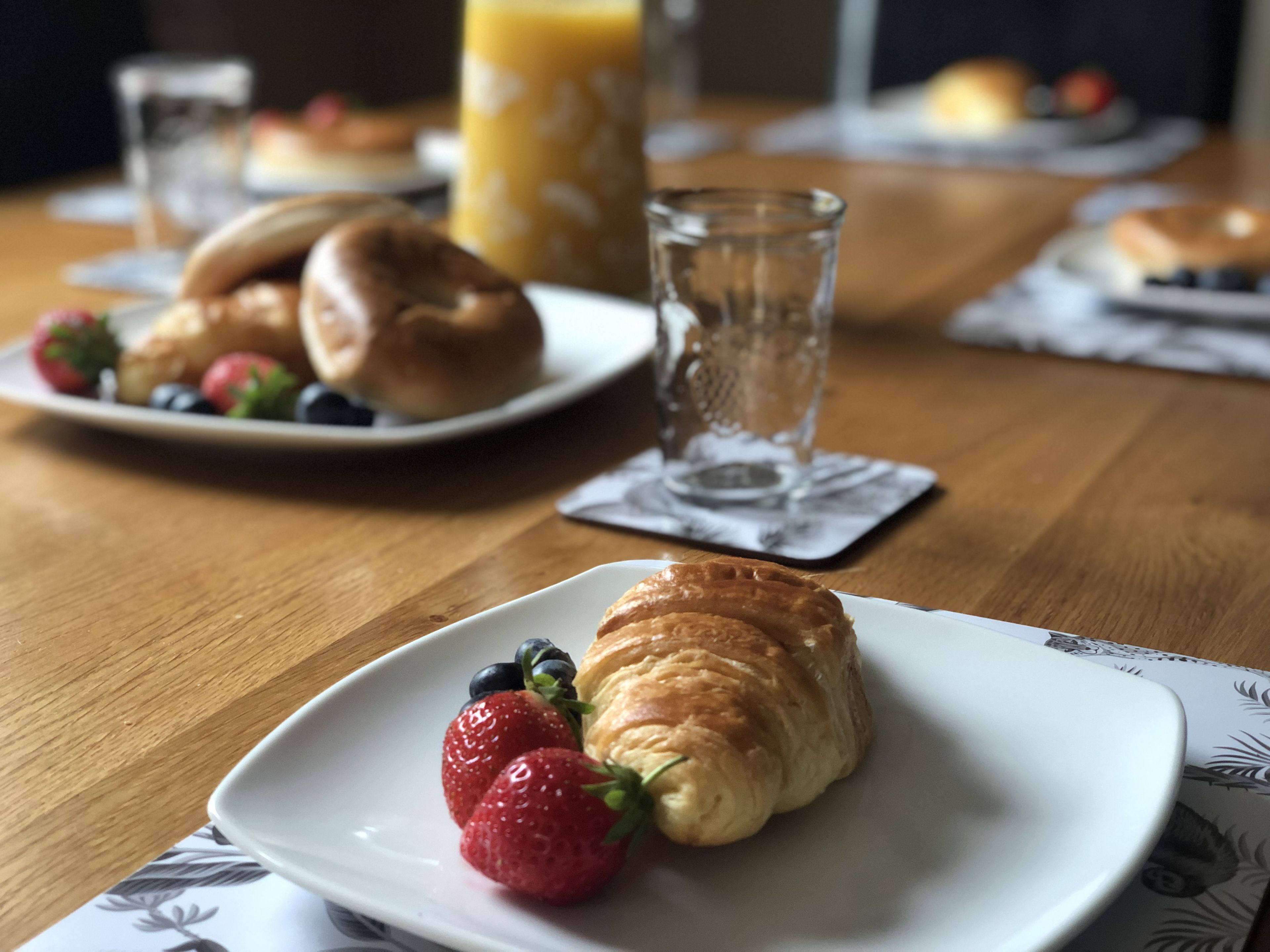 A breakfast setting with croissants, strawberries, and a glass of orange juice on a wooden table.