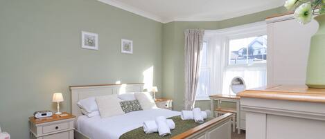 Een netjes ingerichte slaapkamer met een bed, nachtkastjes, een dressoir en een raam met gordijnen.
