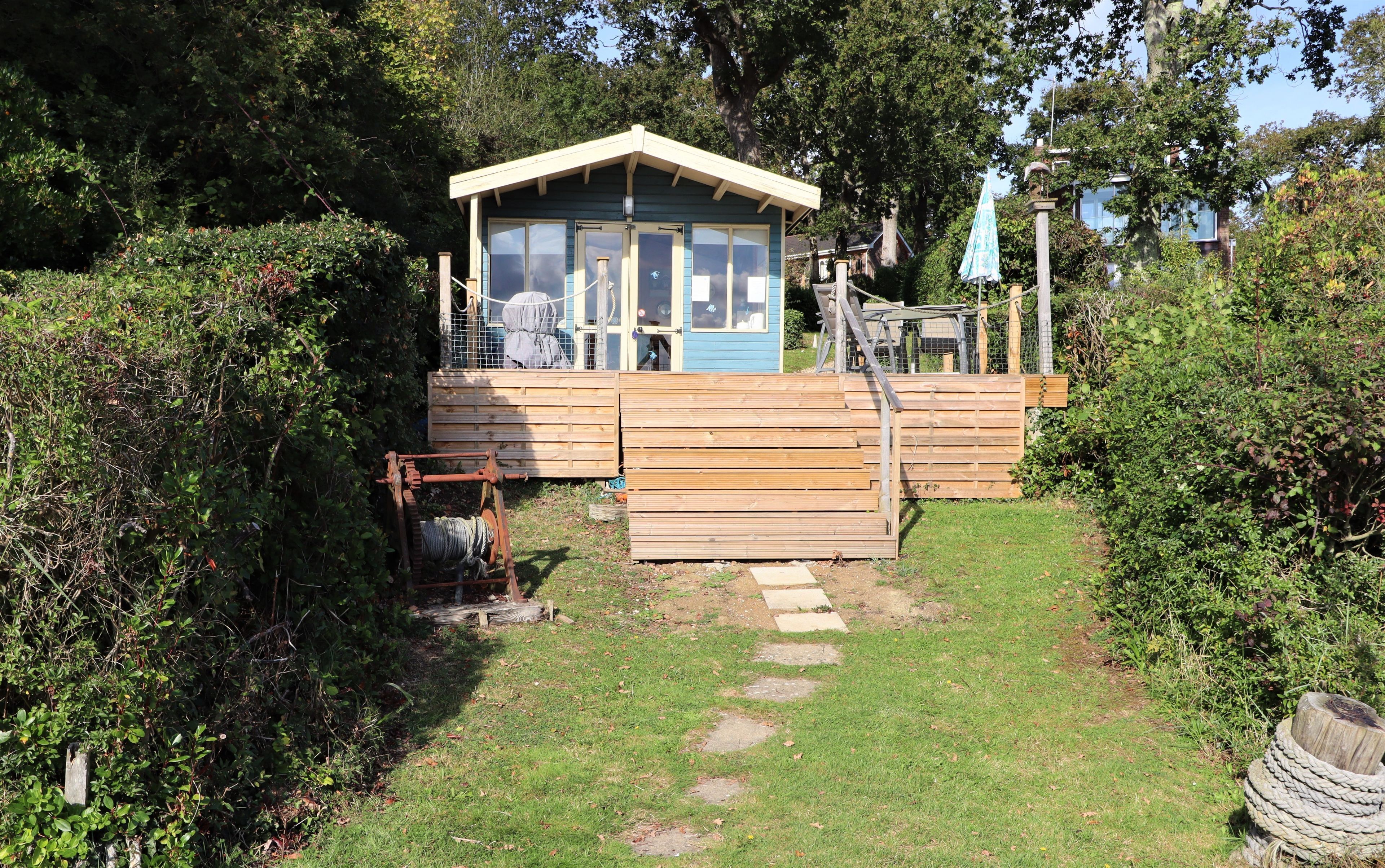 A small wooden cabin with a porch, surrounded by dense greenery.