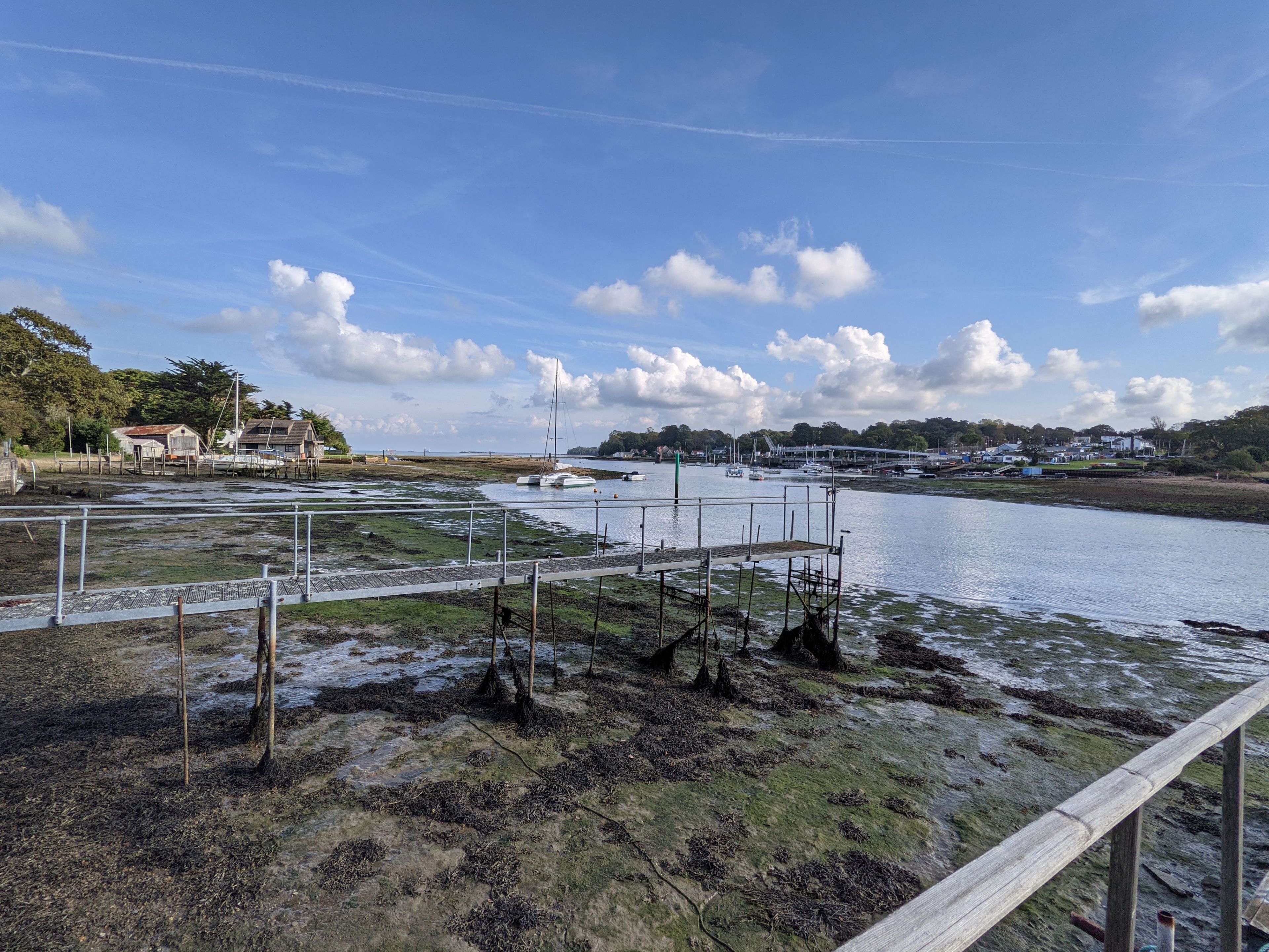 Zona costera con muelle, barcos y un pueblo distante.