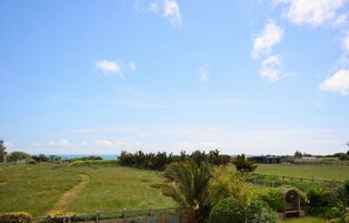 A grassy field with a path, a wooden fence, and a small structure.