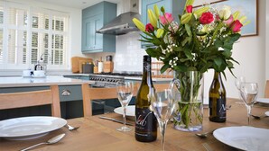 A dining table set with plates, cutlery, wine glasses, and a bottle of wine. - Hope Cottage (Bembridge)