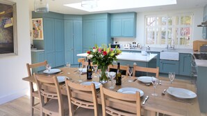 A modern kitchen with teal cabinets, a wooden dining table set for six, and a skylight above. - Hope Cottage (Bembridge)