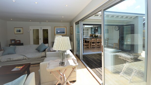 A modern living room with a sofa, a coffee table, and a lamp. There is a glass door leading to a balcony with a wooden deck. - Hope Cottage (Bembridge)