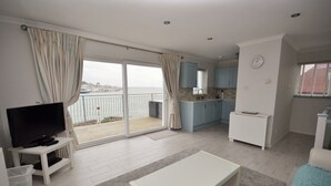 A living room with a TV, a white coffee table, and a sofa. There is a balcony with a view of the sea. - Harbour View (East Cowes)