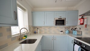 A kitchen with light blue cabinets, a stainless steel sink, a microwave, a toaster, and a fire extinguisher on the wall. - Harbour View (East Cowes)