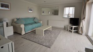 A modern living room with a sofa, coffee table, TV, and a window with curtains. - Harbour View (East Cowes)