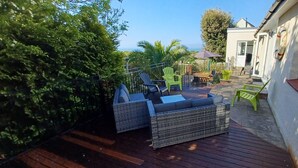 A patio area with wicker furniture, a wooden deck, and a view of the ocean.