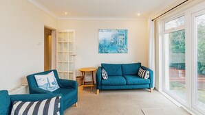 A living room with teal sofas, a small round table, and a large window with a view of greenery.