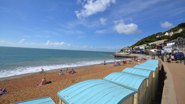 A beach with people relaxing, a pier, and houses along the shore.