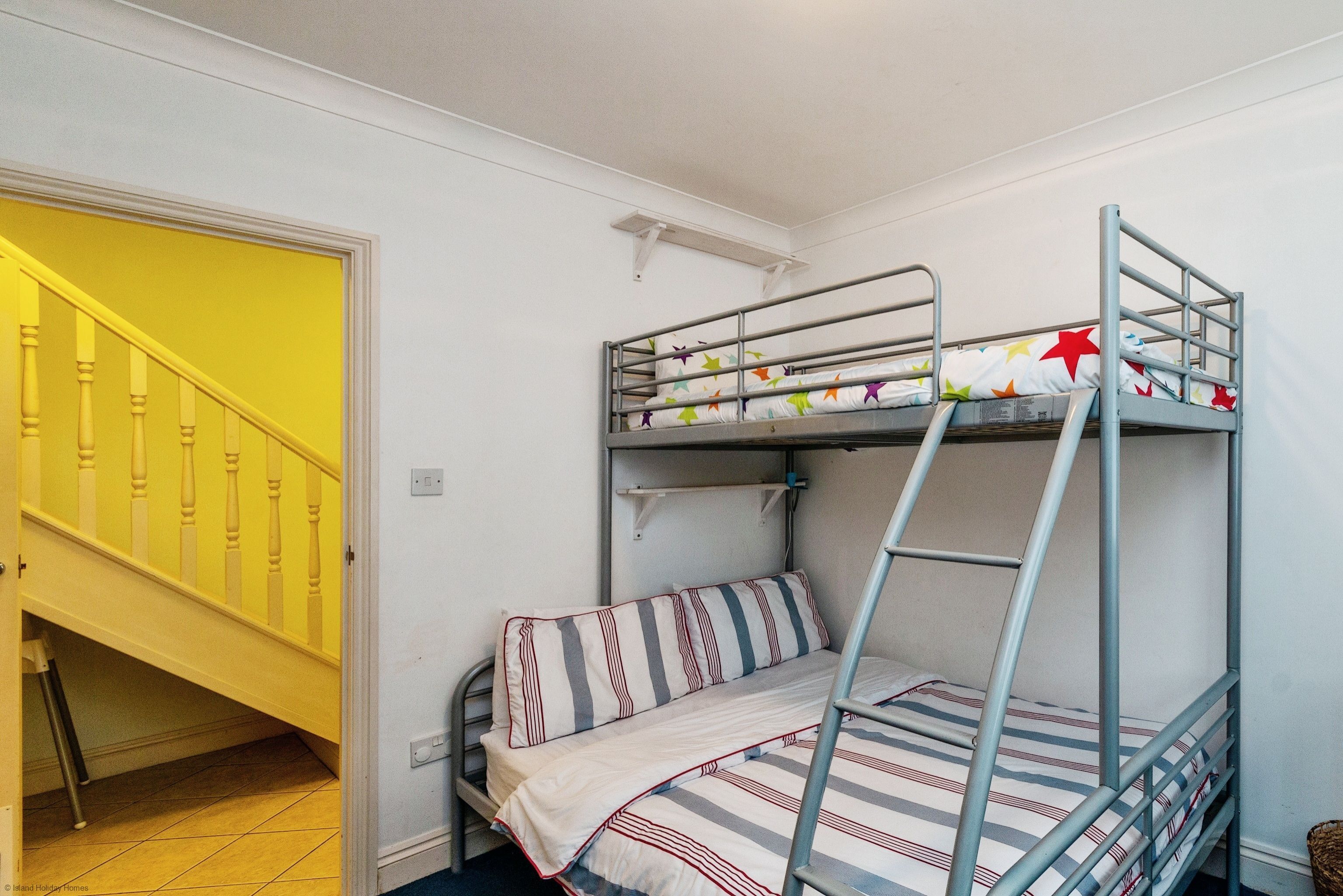 A bunk bed with striped bedding, a small shelf above it, and a yellow staircase in the background.