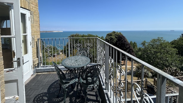 A balcony with a table and chairs, overlooking a coastal view.