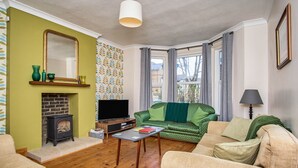 Una sala de estar con chimenea, un sofá verde, un sofá color crema y un televisor.