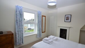Une chambre à coucher comprenant un lit, une commode, une fenêtre avec des rideaux, une armoire et un tableau encadré accroché au mur.