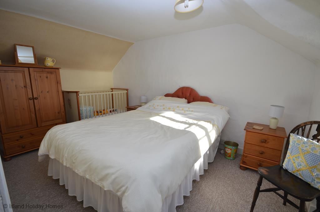 A bedroom with a large bed, wooden wardrobe, and a small bedside table.