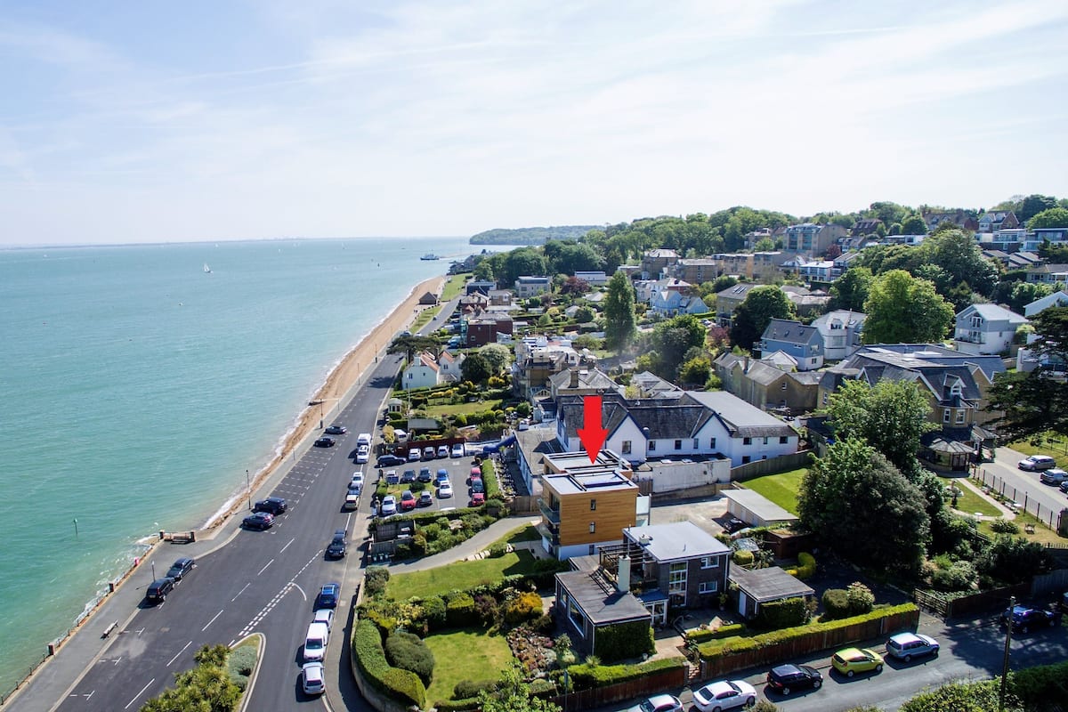 An aerial view of a coastal town with a beach, residential buildings, and a parking area.