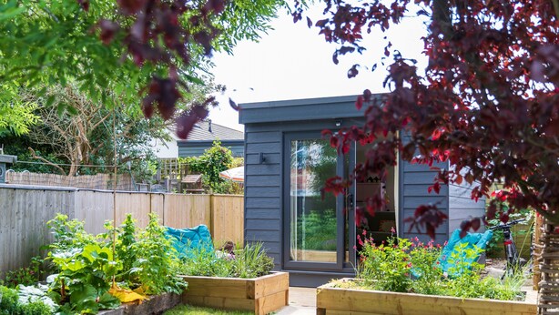 A residential backyard with raised garden beds, a wooden fence, and a sliding glass door leading to a house.