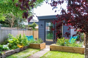 A residential backyard with raised garden beds, a wooden fence, and a sliding glass door leading to a house. - Serendipity (Cowes)