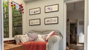 A cozy living room with a patterned floor, a grey sofa with multiple cushions, and framed pictures on the wall.