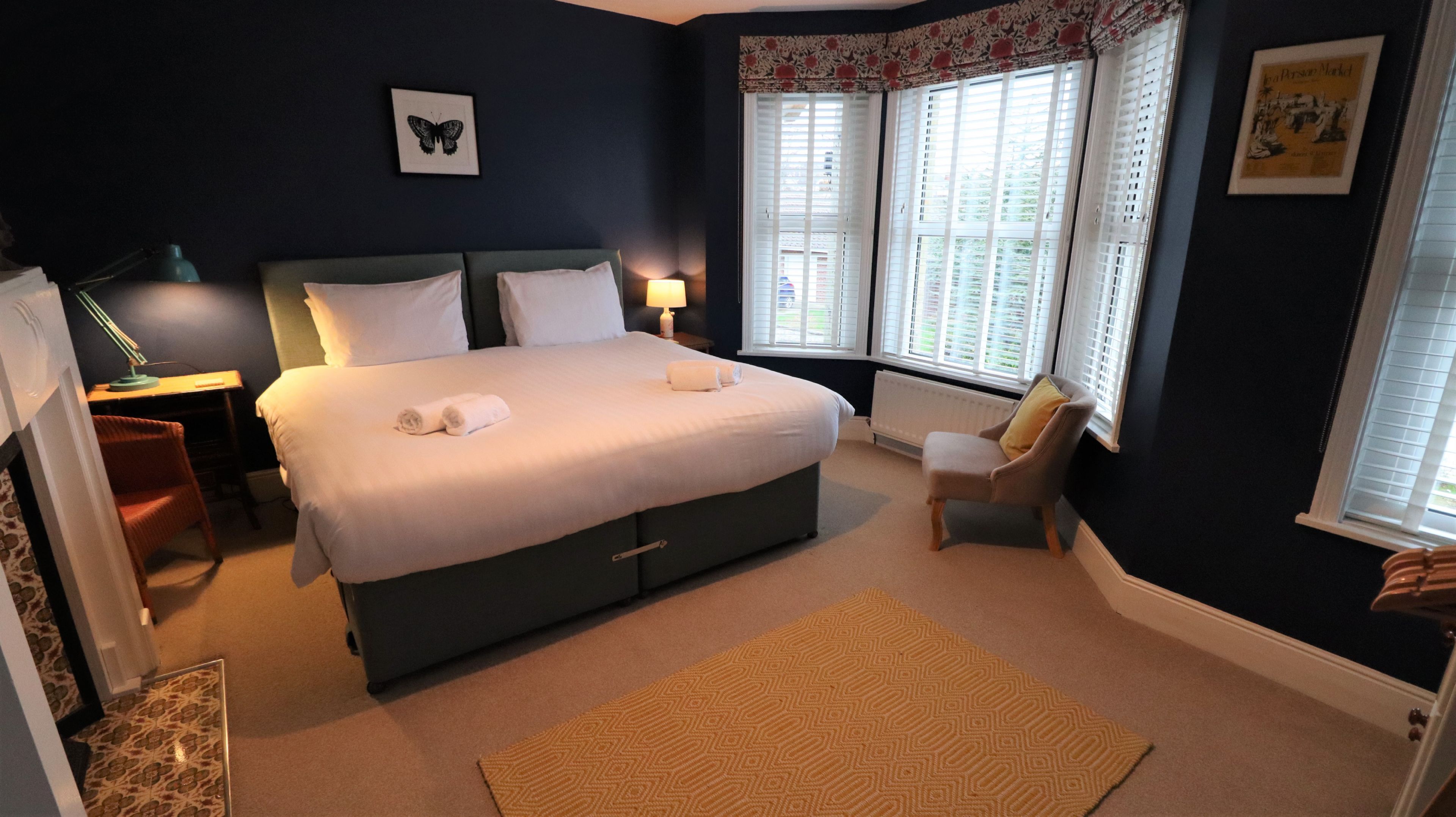 A neatly arranged bedroom with a large bed, a chair, a desk, and a window with blinds.