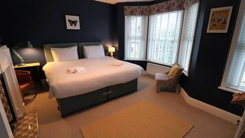 A neatly arranged bedroom with a large bed, a chair, a desk, and a window with blinds.