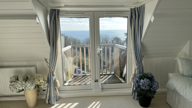 A room with a view of the sea, a balcony with a railing, a bed, and two potted plants. - Mole Cottage (Shanklin)