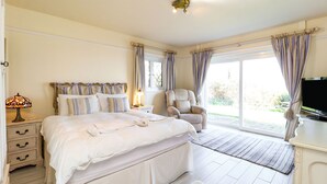 A bedroom with a bed, bedside tables, a chair, a TV, and a large window with curtains. - Mole Cottage (Shanklin)