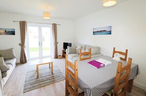 Ein gemütliches Zimmer mit Esstisch, Stühlen, einer Couch und einem Fernseher.