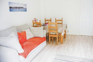 A living room with a sofa, a dining table with chairs, a picture on the wall, and a door.
