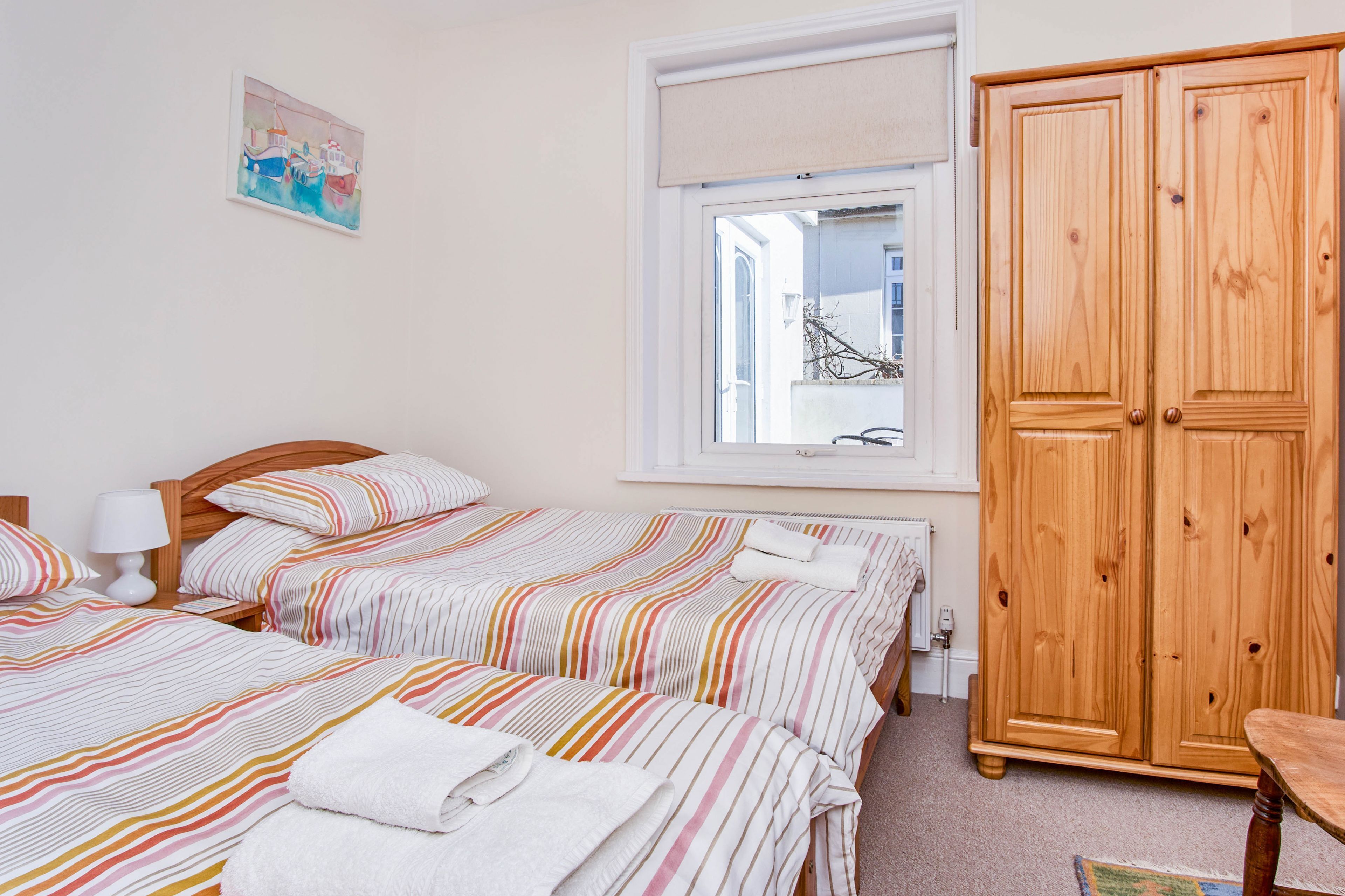 A hotel room with two beds, a wooden wardrobe, a window with a view, and a painting on the wall.