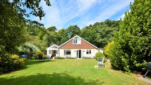 Ein zweistöckiges Haus mit gepflegtem Rasen, einer Terrasse mit Gartenmöbeln und einem Grill.