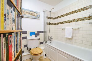 A bathroom with a toilet, shower, bathtub, and a bookshelf with books. - The Old Signal House (Ventnor)