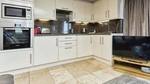 Une cuisine moderne avec des meubles blancs, un four Bosch, un four à micro-ondes, un grille-pain et un téléviseur à écran plat posé sur un meuble en bois.