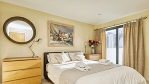 Une chambre bien rangée, avec un lit, une table de chevet, une commode et un tableau accroché au mur.