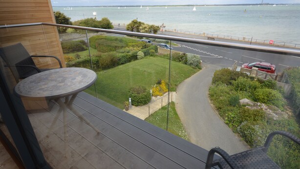 Un balcon donnant sur un plan d’eau, une route et de la verdure.