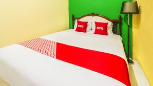 Ein Bett mit weißer und roter Bettdecke, zwei rote Kissen mit dem Aufdruck "OYO", ein hölzernes Kopfstück und eine Stehlampe.