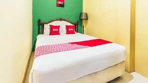 Un lit recouvert d’une couvre-lit à motifs rouges et blancs, deux oreillers rouges ornés du mot « OVO », et un panneau « SMILE » accroché au mur.