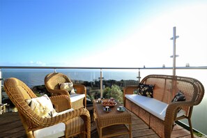 Un sofá y sillones de mimbre en un balcón con vista al mar.
