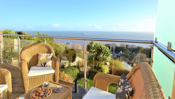 Un balcon agrémenté de meubles en osier, d’une table en verre et offrant une vue sur la mer.