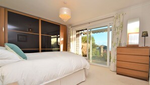 Une chambre à coucher avec un grand lit, une commode, un lustre et une porte-fenêtre coulissante donnant sur un balcon.