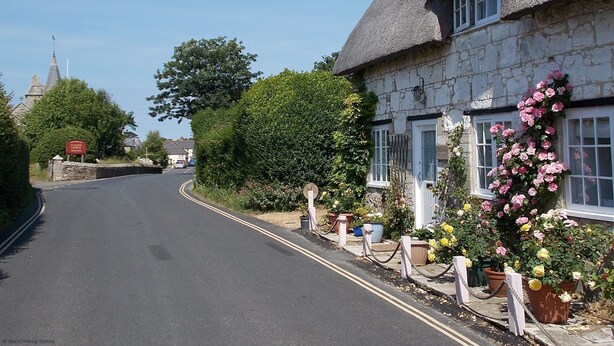 A narrow street with a stone building featuring a thatched roof and potted plants.