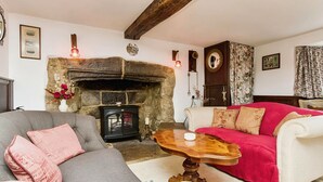 A cozy living room with a stone fireplace, a grey sofa, a red and white armchair, and a wooden coffee table. - Ye Olde Cottage (Ventnor)