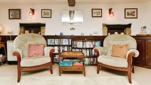 A cozy living room with two armchairs, a small wooden table, and a bookshelf filled with books. - Ye Olde Cottage (Ventnor)