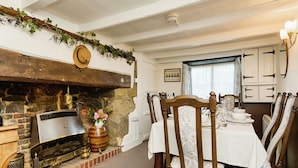 A dining area with a fireplace, wooden chairs, a table set for a meal, and a window with curtains. - Ye Olde Cottage (Ventnor)