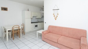 Un salon avec un canapé blanc, une table à manger avec des chaises, un coin cuisine et une décoration murale représentant la lune.