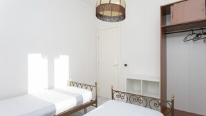 Une chambre avec deux lits simples, une armoire et un luminaire suspendu.