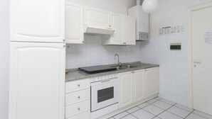 Une cuisine avec des meubles blancs, une cuisinière, un évier et un dosseret de carrelage blanc.