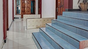 Een hotel lobby met een betegelde vloer, een houten trap en een receptiebalie.
